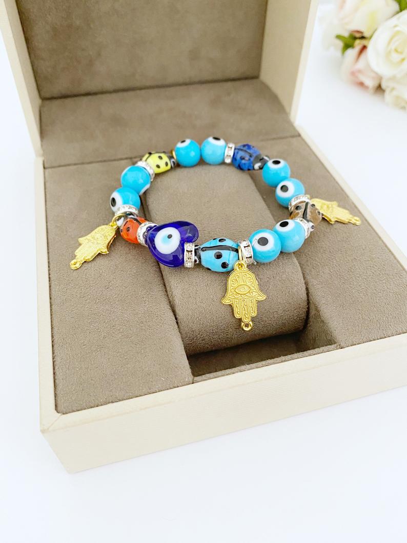 Evil Eye Bracelet featuring turquoise beads, gold hamsa charm, and ladybug charm, showcasing a stylish and protective design.