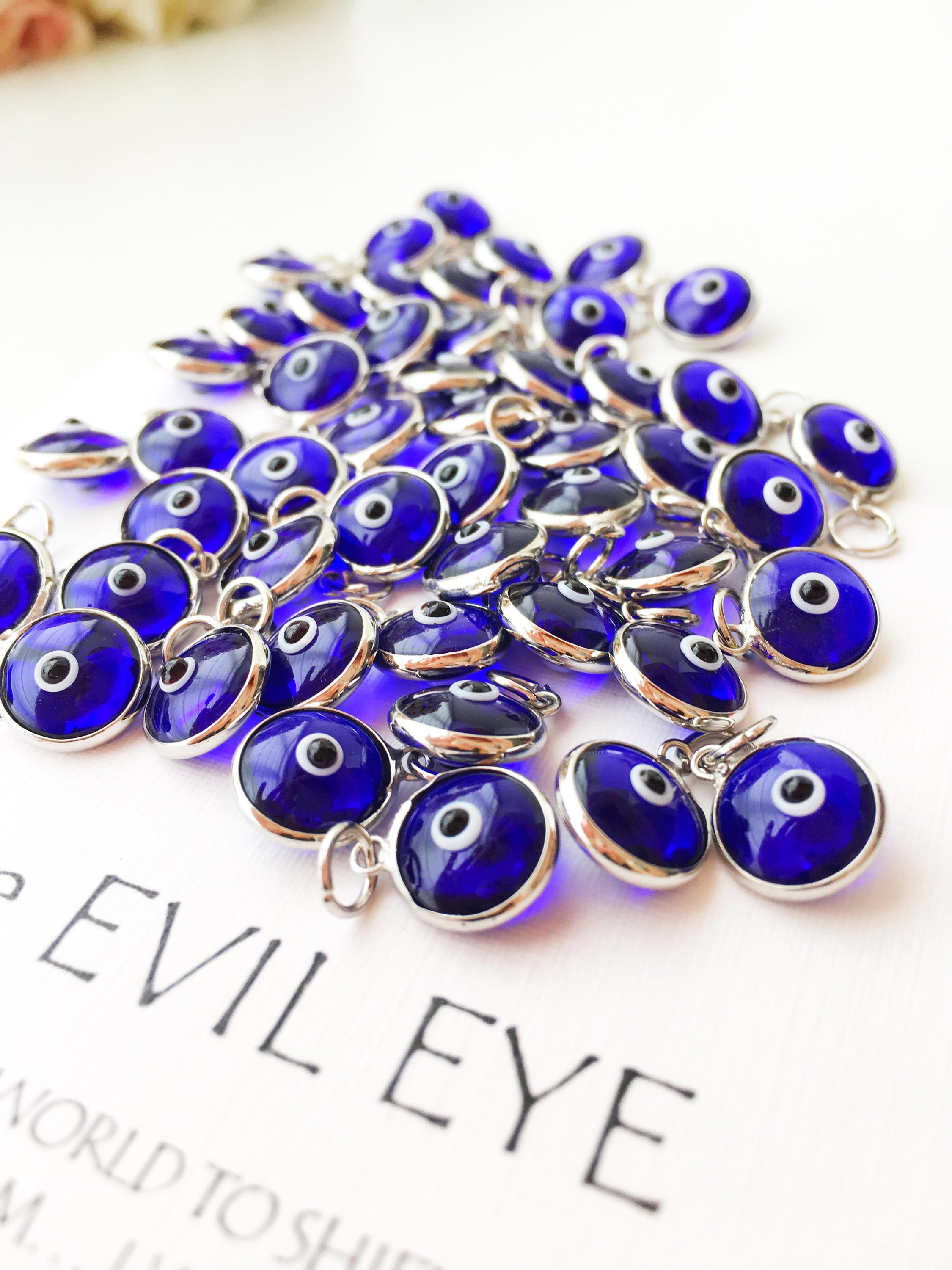A collection of blue evil eye charms made from glass, featuring silver and gold finishing options, showcasing both-sided designs.