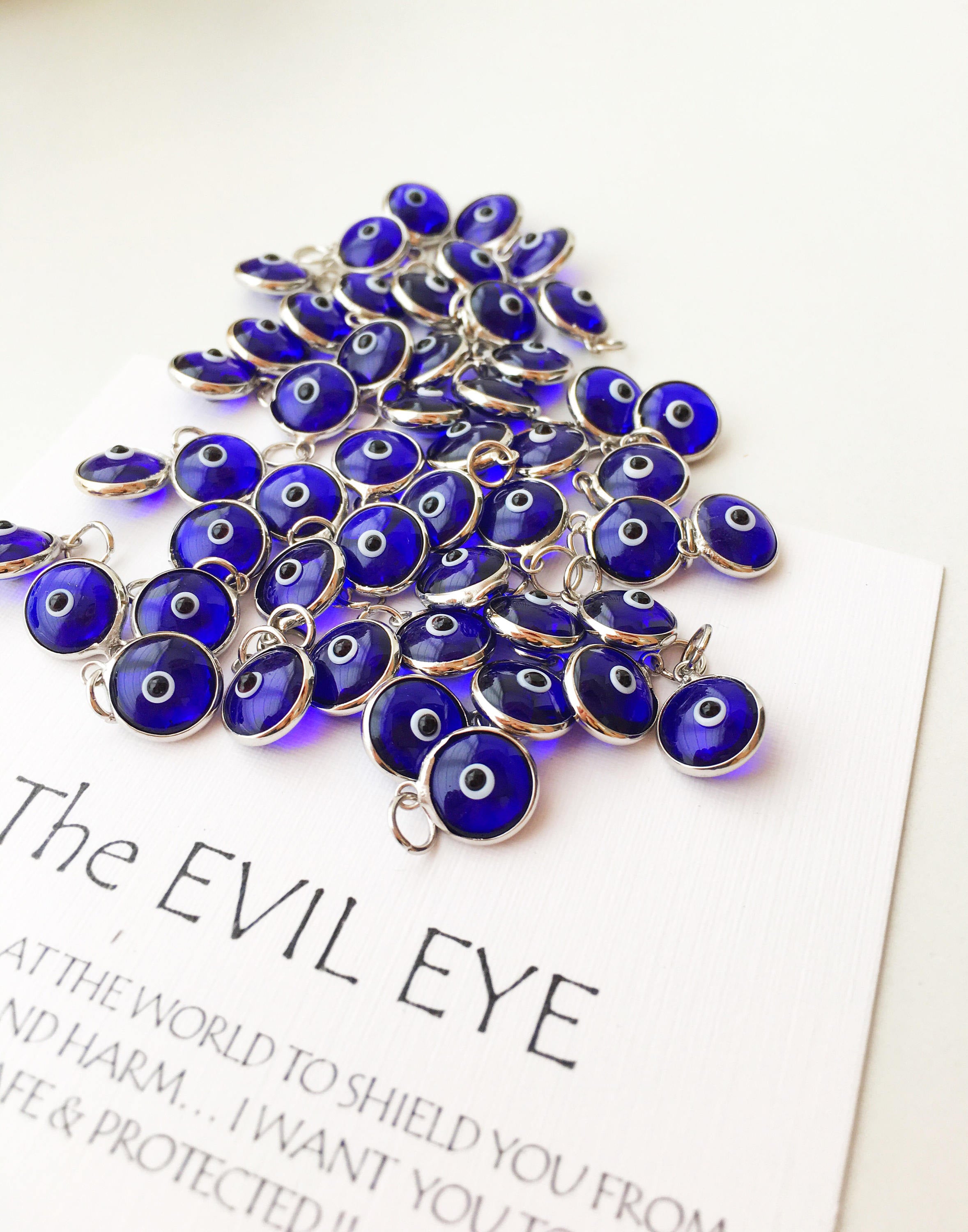 A collection of blue evil eye charms made from glass, featuring silver and gold finishing options, showcasing both-sided designs.