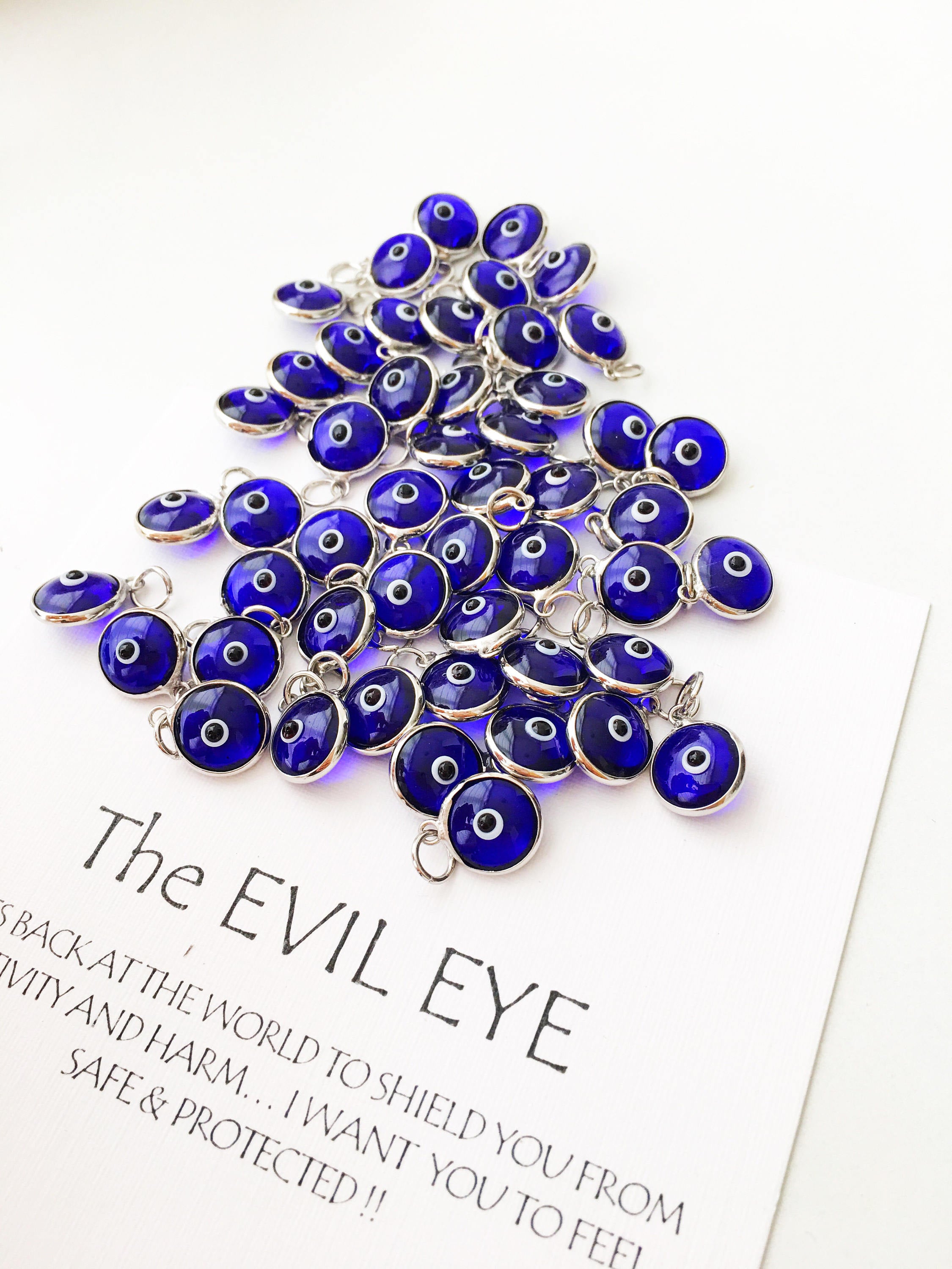A collection of blue evil eye charms made from glass, featuring silver and gold finishing options, showcasing both-sided designs.