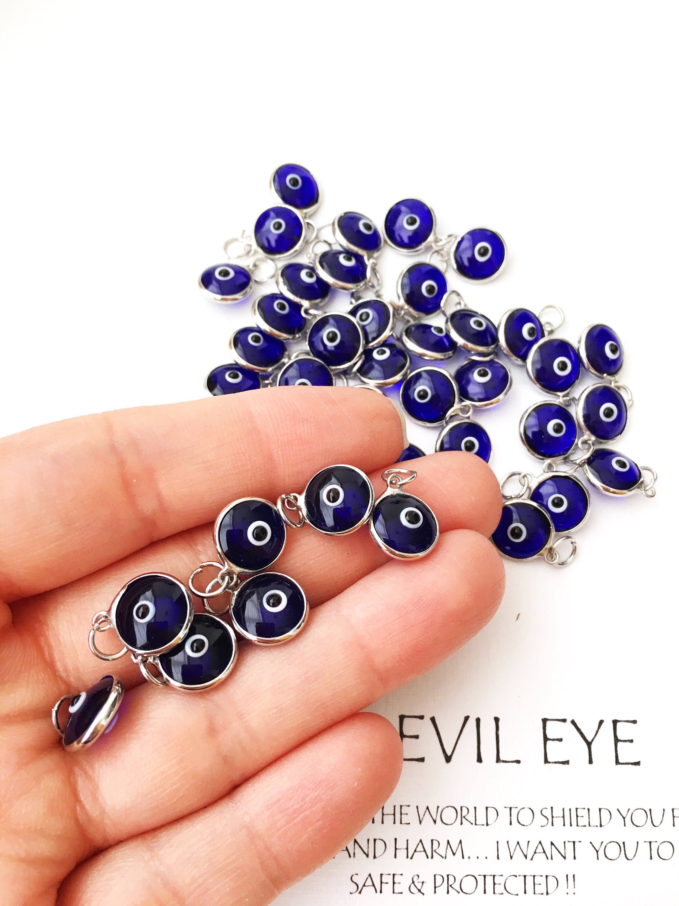 A collection of blue evil eye charms made from glass, featuring silver and gold finishing options, showcasing both-sided designs.