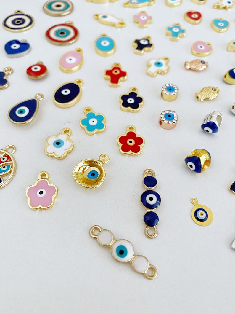 A collection of 63 different styles of evil eye charms in bulk, featuring gold, silver, and enamel designs.