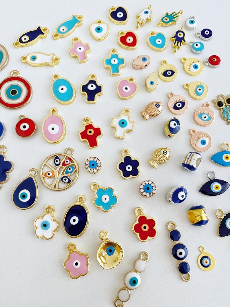 A collection of 63 different styles of evil eye charms in bulk, featuring gold, silver, and enamel designs.