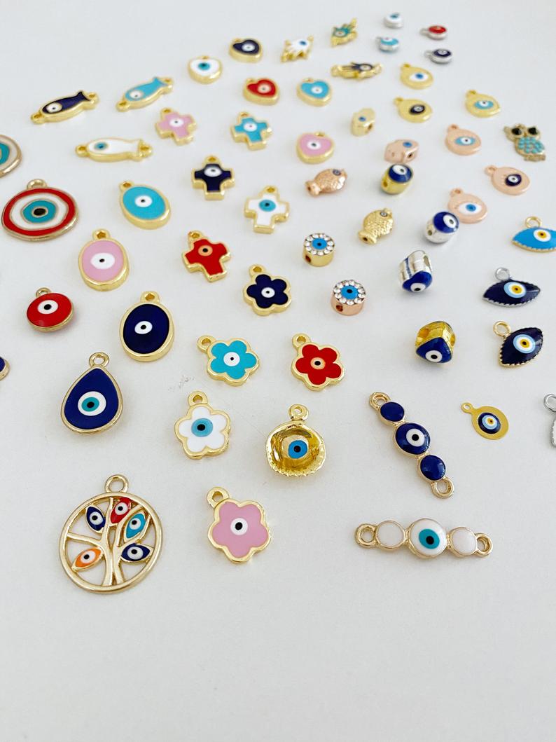A collection of 63 different styles of evil eye charms in bulk, featuring gold, silver, and enamel designs.
