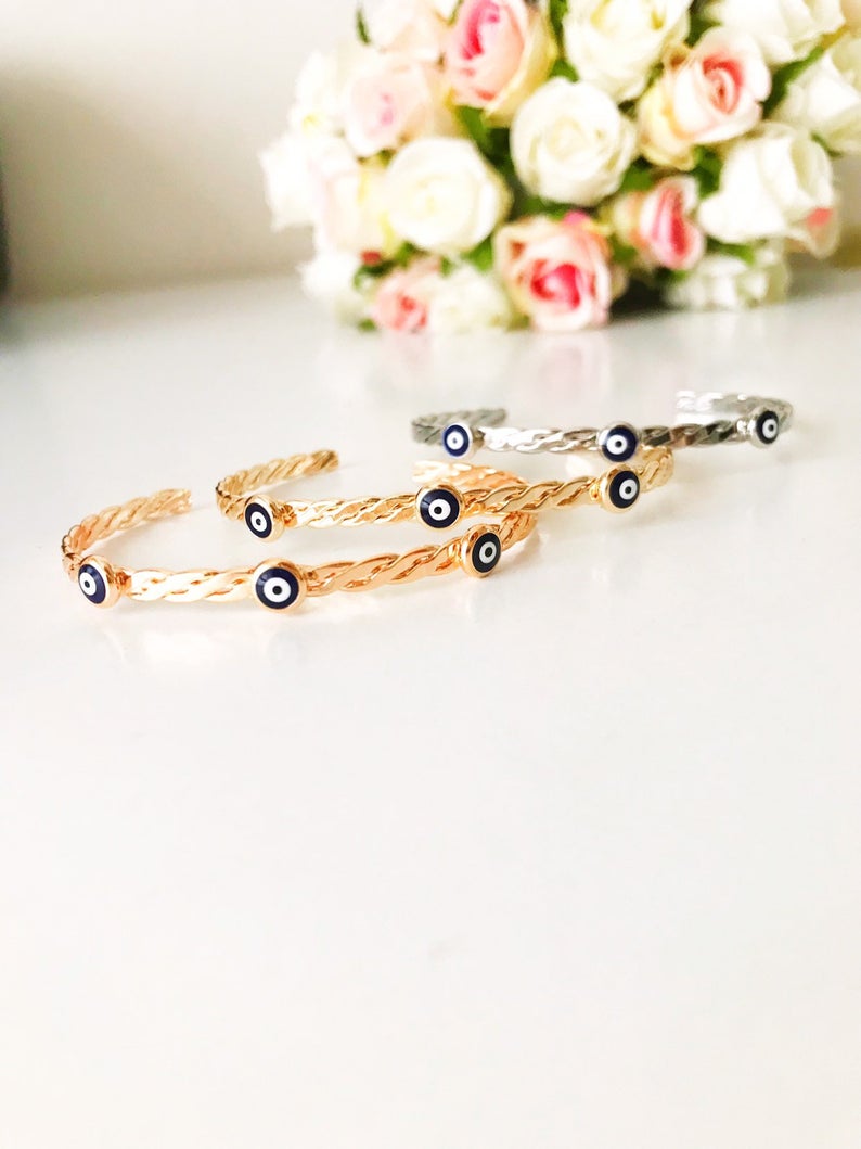 Evil Eye Cuff Bracelet featuring a blue Greek evil eye bead, available in rose gold, gold, and silver finishes, showcasing its adjustable design.