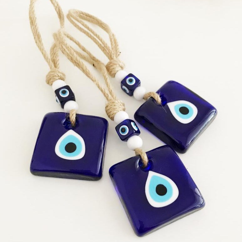 Handmade macrame evil eye wall hanging featuring blue glass beads and tiny white beads, symbolizing protection and good luck.