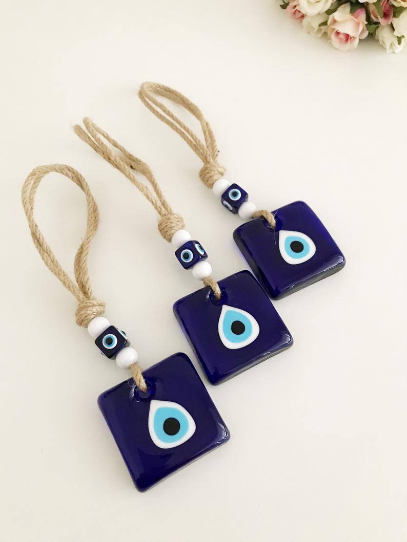 Handmade macrame evil eye wall hanging featuring blue glass beads and tiny white beads, symbolizing protection and good luck.