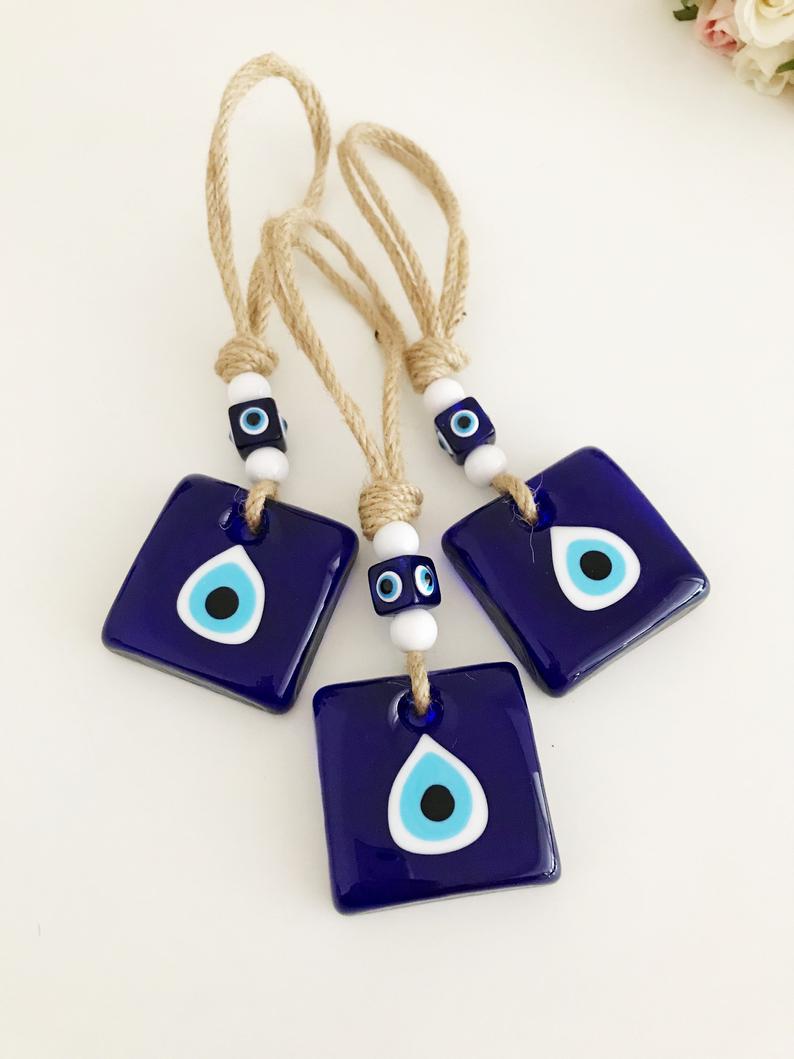 Handmade macrame evil eye wall hanging featuring blue glass beads and tiny white beads, symbolizing protection and good luck.