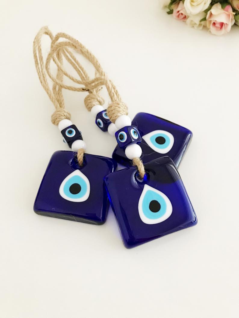 Handmade macrame evil eye wall hanging featuring blue glass beads and tiny white beads, symbolizing protection and good luck.