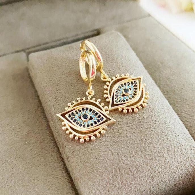 A pair of elegant gold evil eye hoop earrings featuring sparkling zirconia accents, showcasing a unique dangle design.