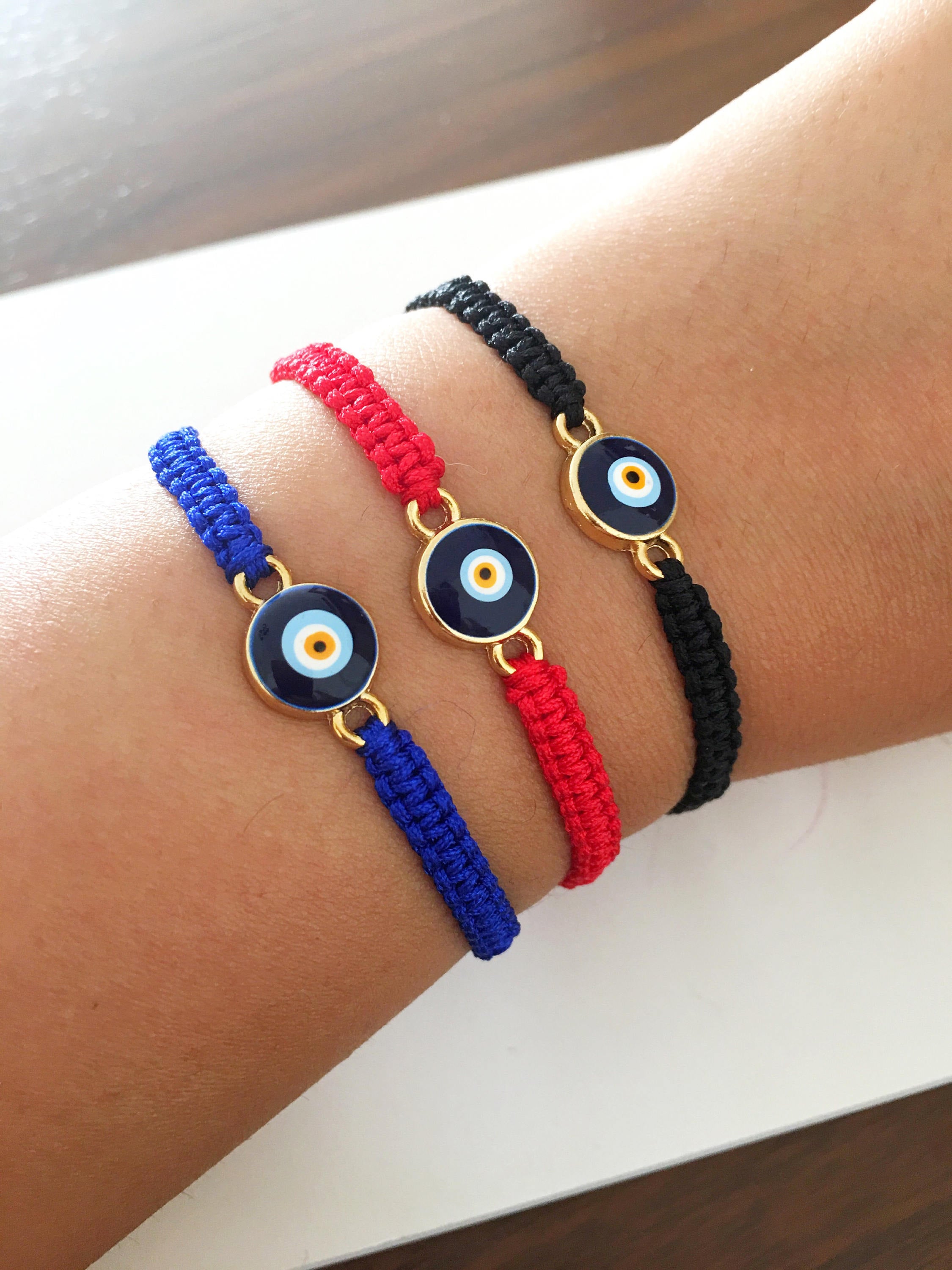 Handmade macrame evil eye bracelet in black, blue, and red strings, featuring a central evil eye charm for protection.