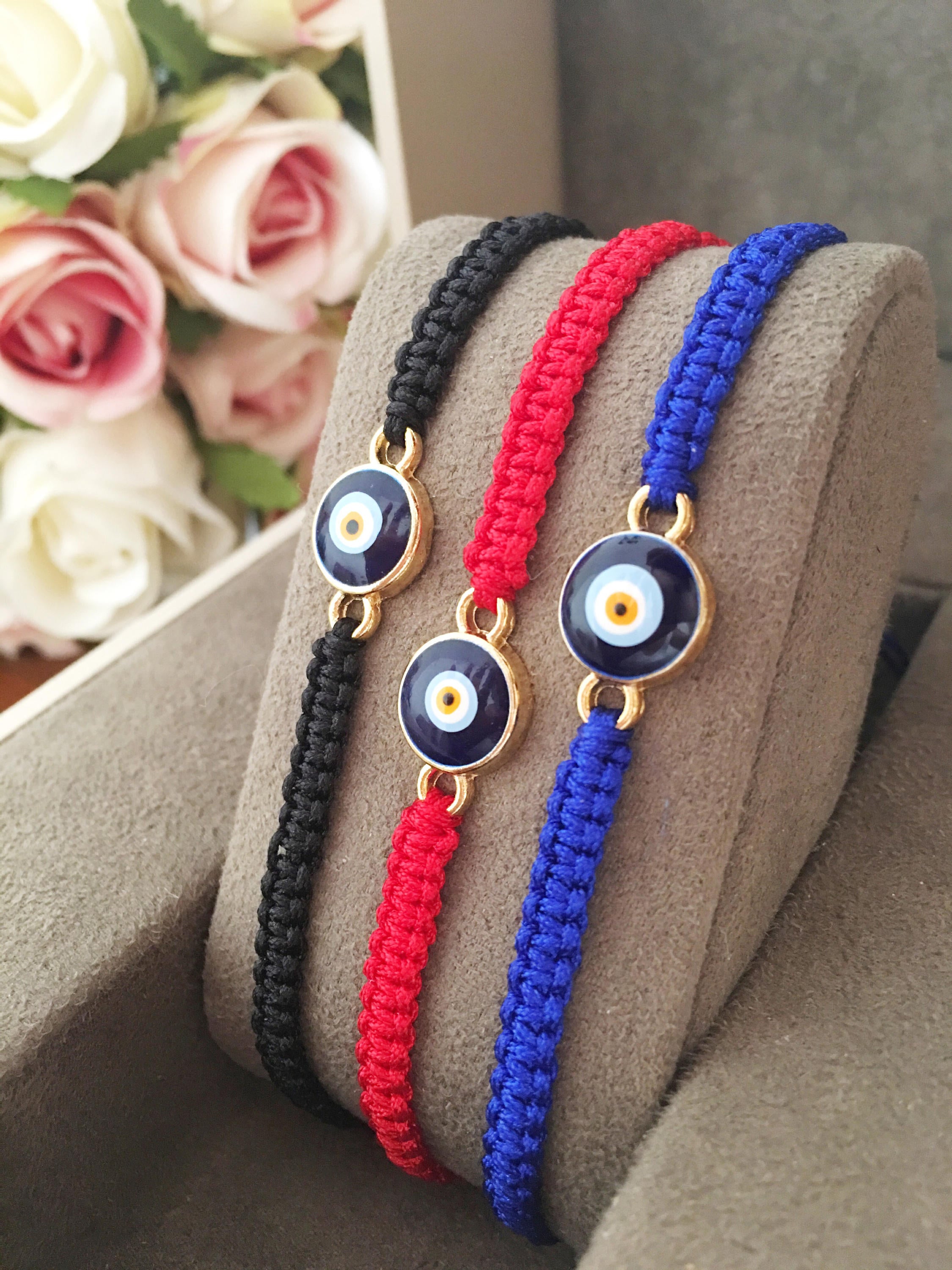 Handmade macrame evil eye bracelet in black, blue, and red strings, featuring a central evil eye charm for protection.