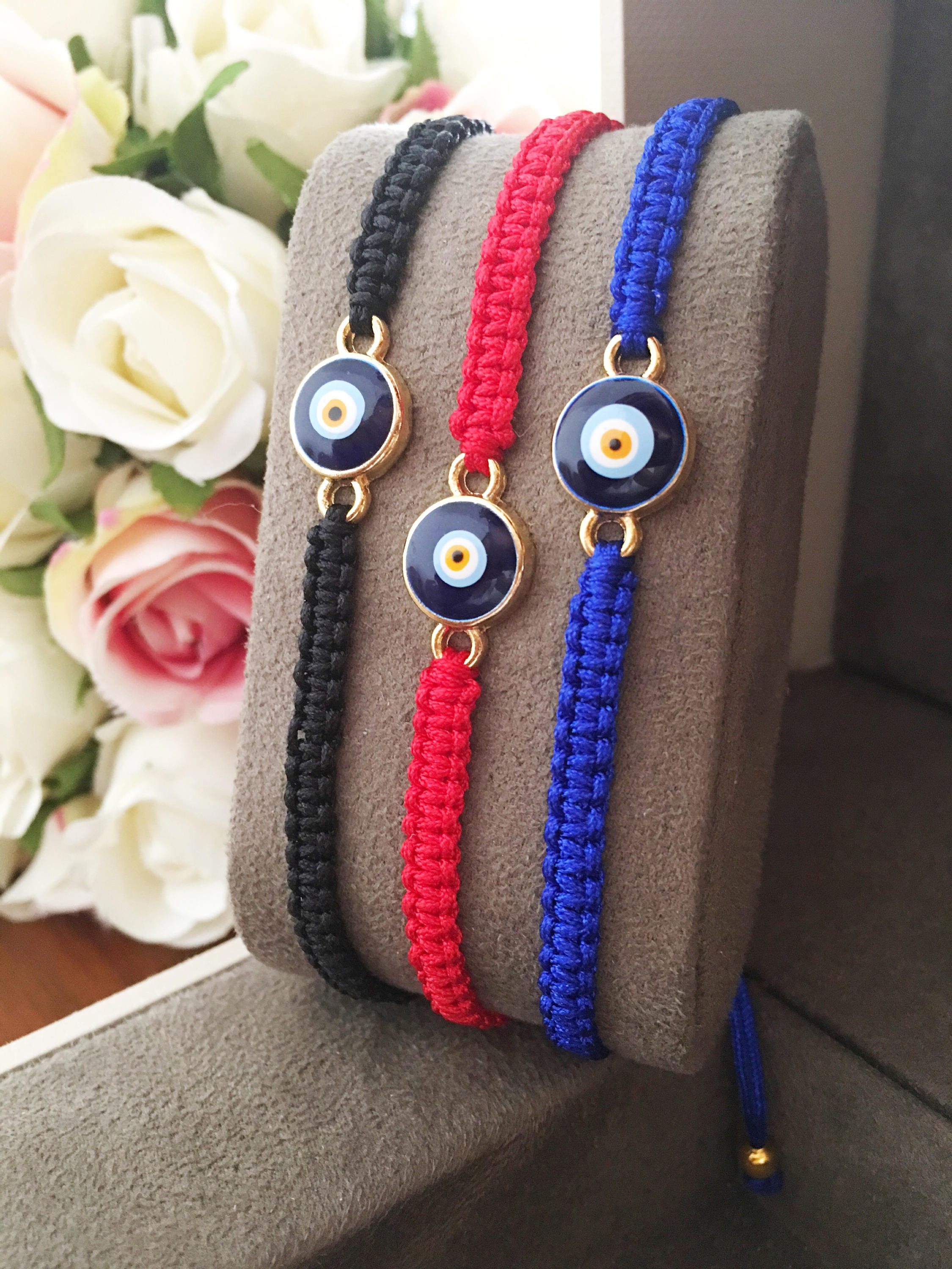 Handmade macrame evil eye bracelet in black, blue, and red strings, featuring a central evil eye charm for protection.
