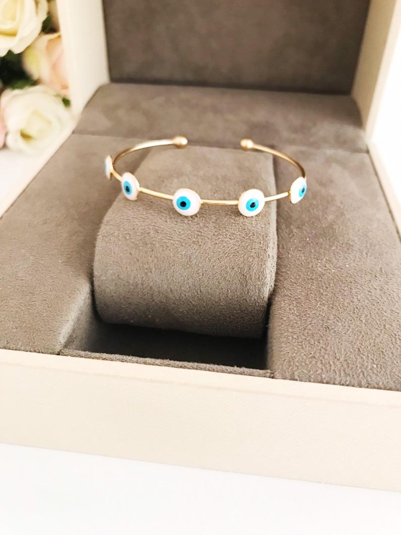 Handmade Evil Eye Jewelry including a white evil eye bracelet, cuff bracelet, and adjustable ring, symbolizing protection and luck.