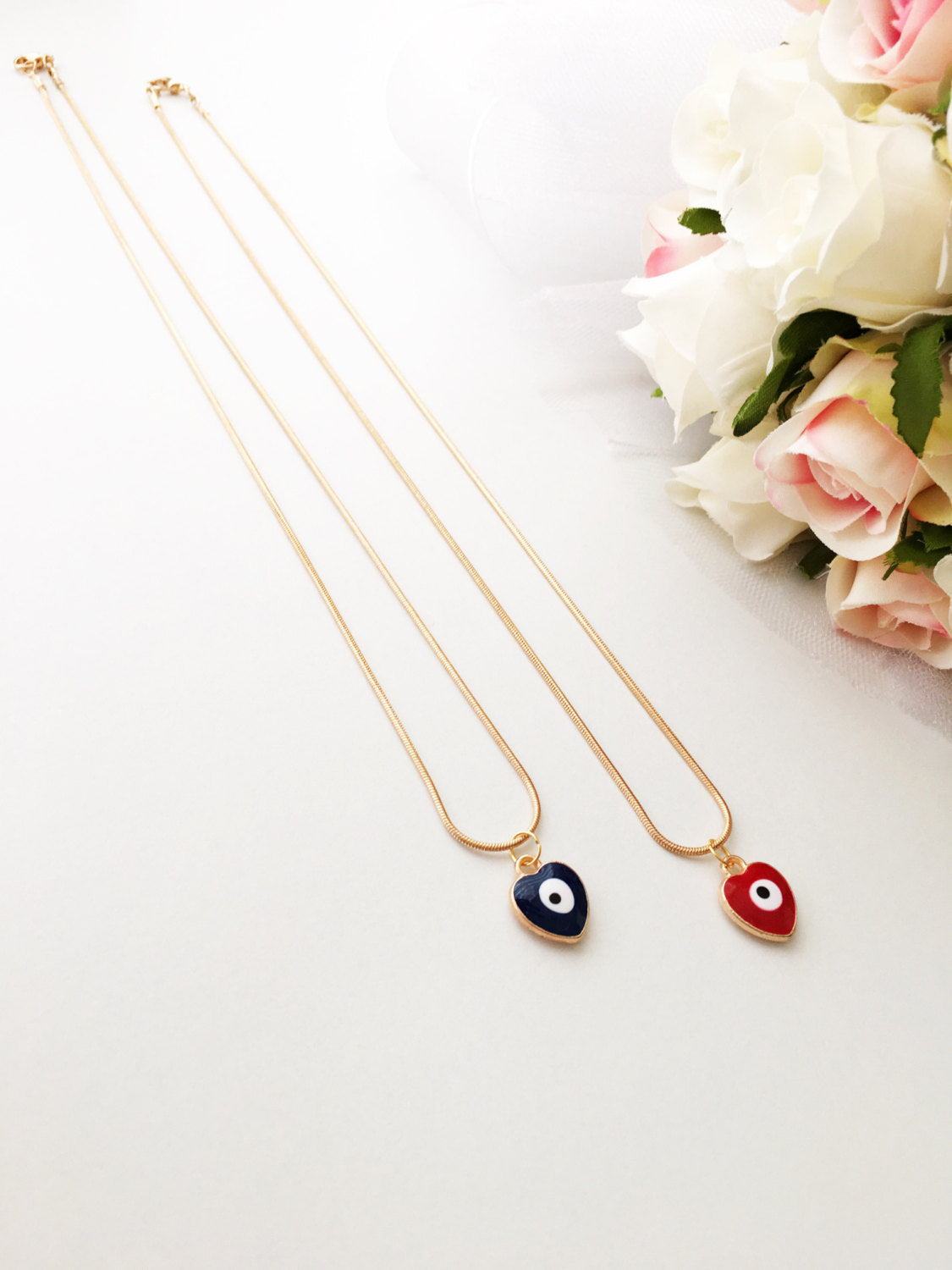Handmade evil eye necklace featuring a heart charm in red and dark blue enamel with a 22K gold plated chain.