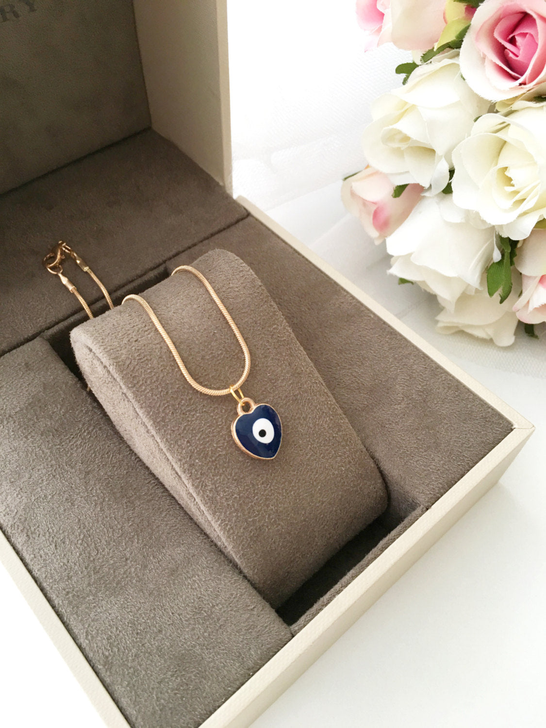 Handmade evil eye necklace featuring a heart charm in red and dark blue enamel with a 22K gold plated chain.
