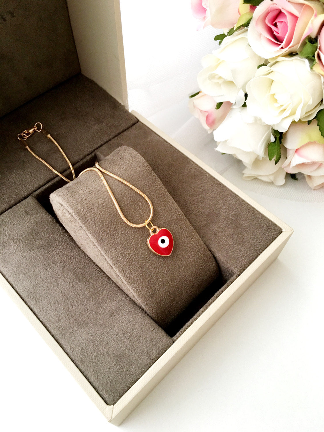 Handmade evil eye necklace featuring a heart charm in red and dark blue enamel with a 22K gold plated chain.