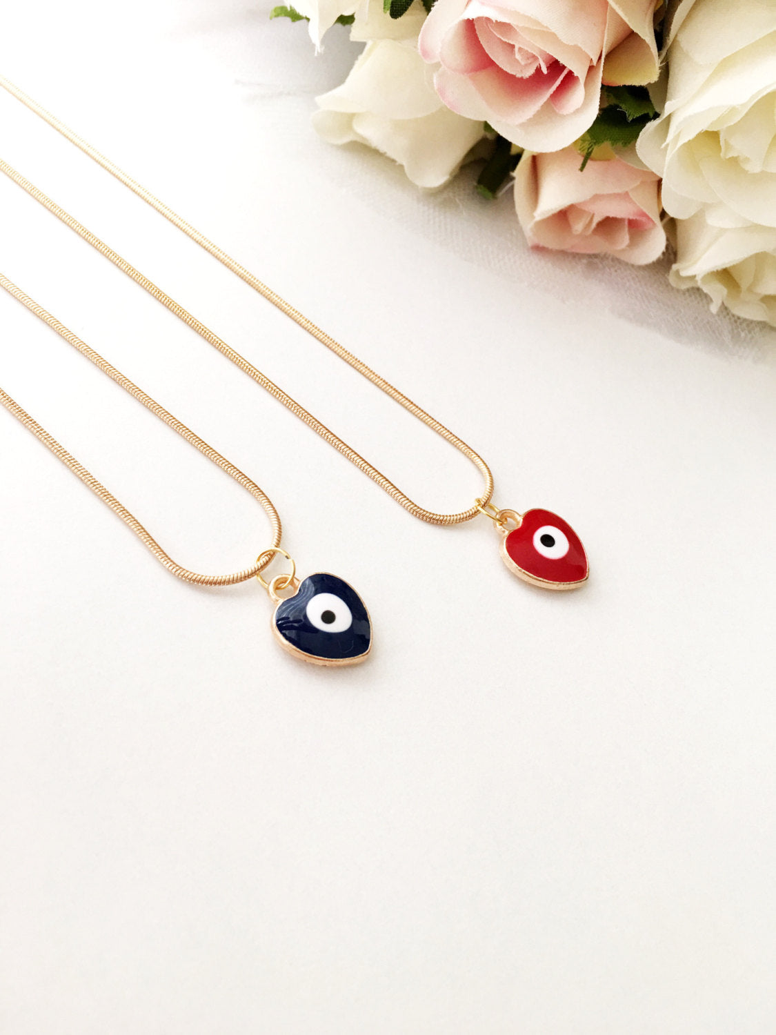 Handmade evil eye necklace featuring a heart charm in red and dark blue enamel with a 22K gold plated chain.