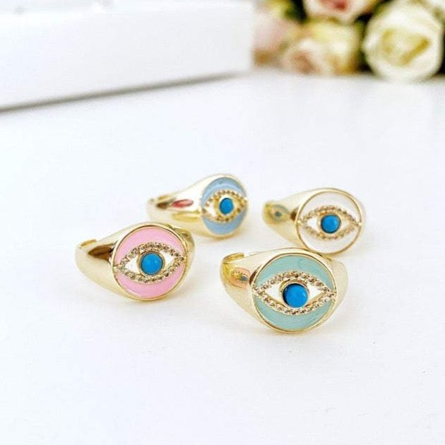 A collection of Evil Eye Signet Rings featuring gold bands and blue zircon charms, showcasing their adjustable and stackable design.