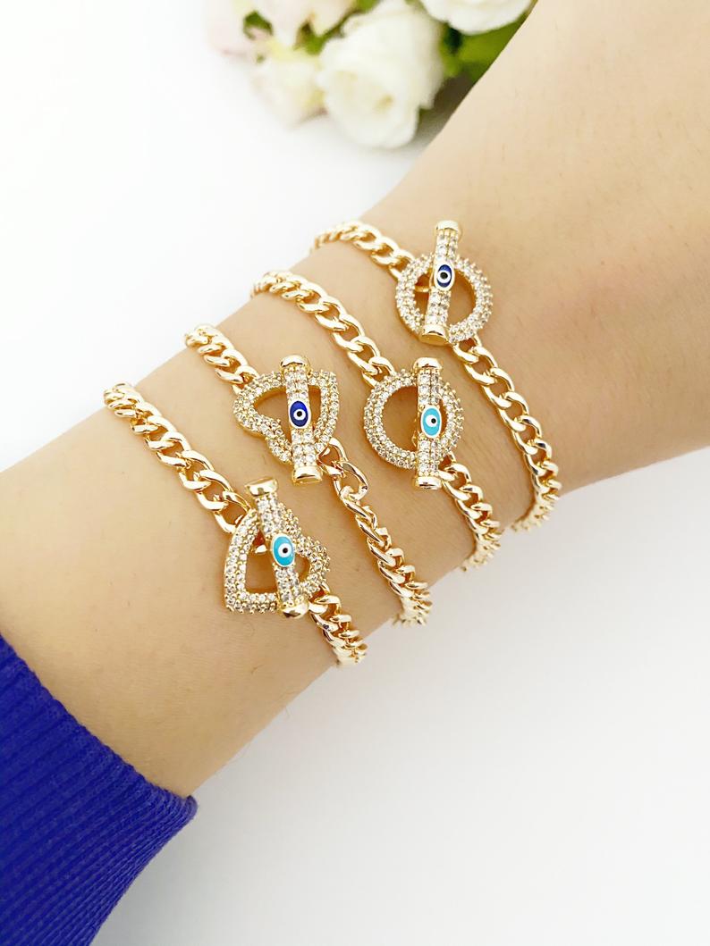 Evil Eye Toggle Bracelet featuring a gold chain, heart charm, and customizable evil eye colors, showcasing its elegant design and handmade quality.