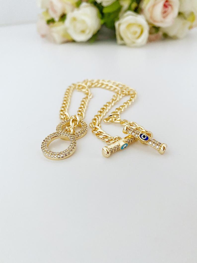 Evil Eye Toggle Bracelet featuring a gold chain, heart charm, and customizable evil eye colors, showcasing its elegant design and handmade quality.