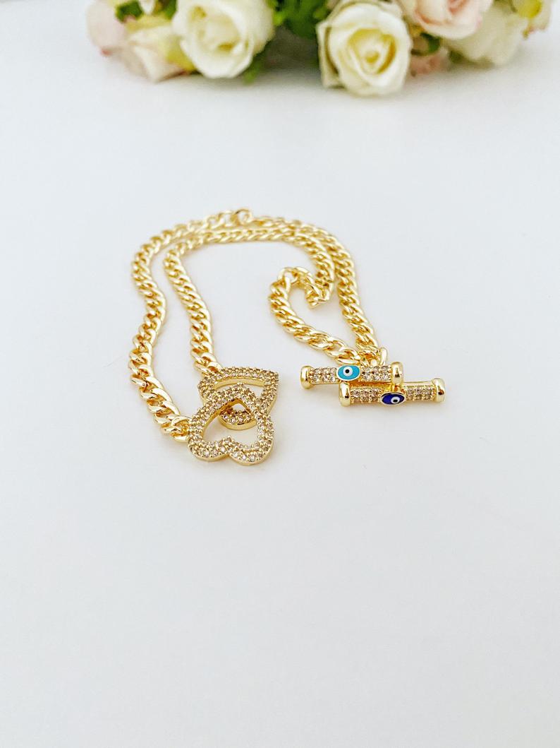 Evil Eye Toggle Bracelet featuring a gold chain, heart charm, and customizable evil eye colors, showcasing its elegant design and handmade quality.