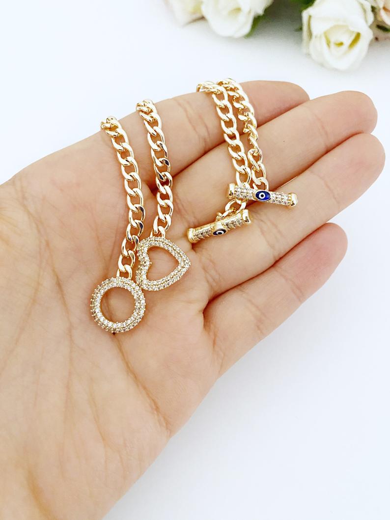 Evil Eye Toggle Bracelet featuring a gold chain, heart charm, and customizable evil eye colors, showcasing its elegant design and handmade quality.