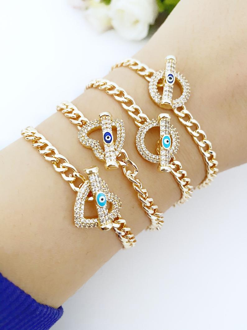 Evil Eye Toggle Bracelet featuring a gold chain, heart charm, and customizable evil eye colors, showcasing its elegant design and handmade quality.