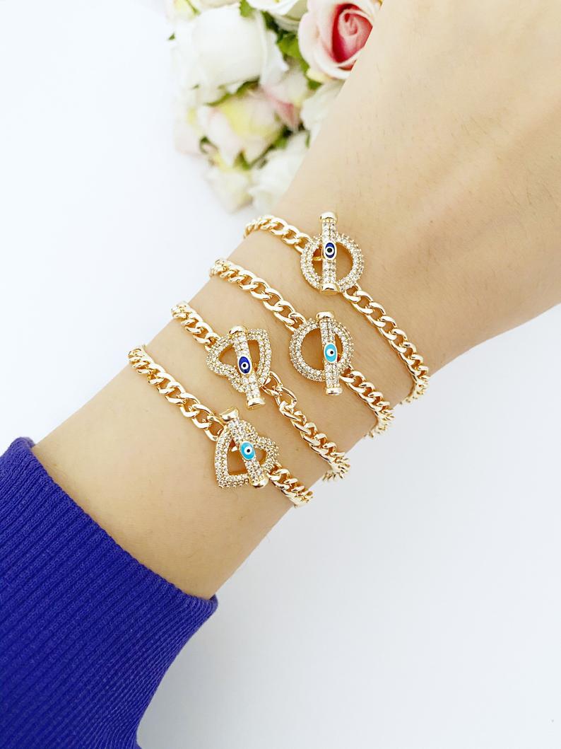 Evil Eye Toggle Bracelet featuring a gold chain, heart charm, and customizable evil eye colors, showcasing its elegant design and handmade quality.