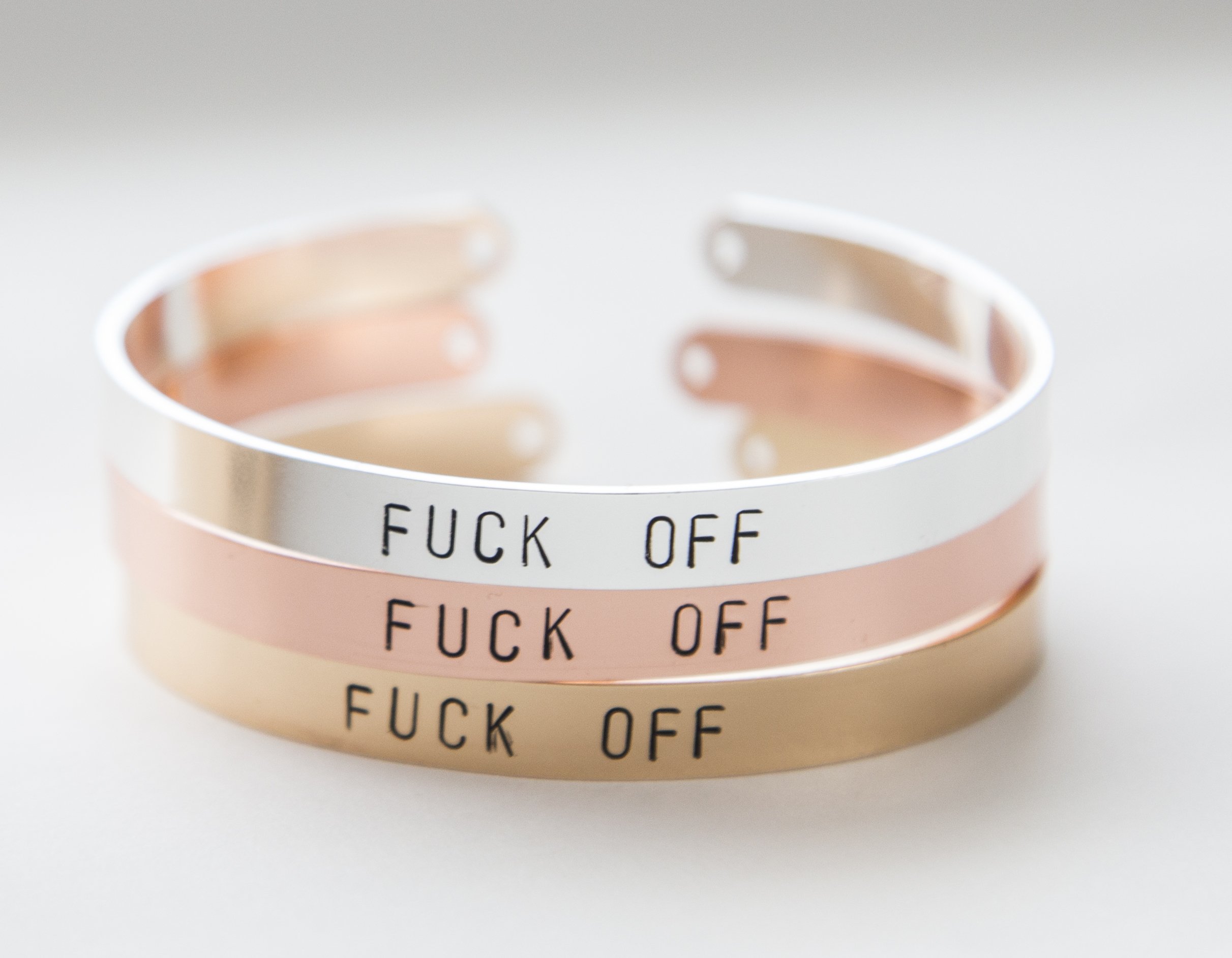 A hand-stamped gold plated cuff bracelet with the phrase 'F off', showcasing its unique design and adjustable size.