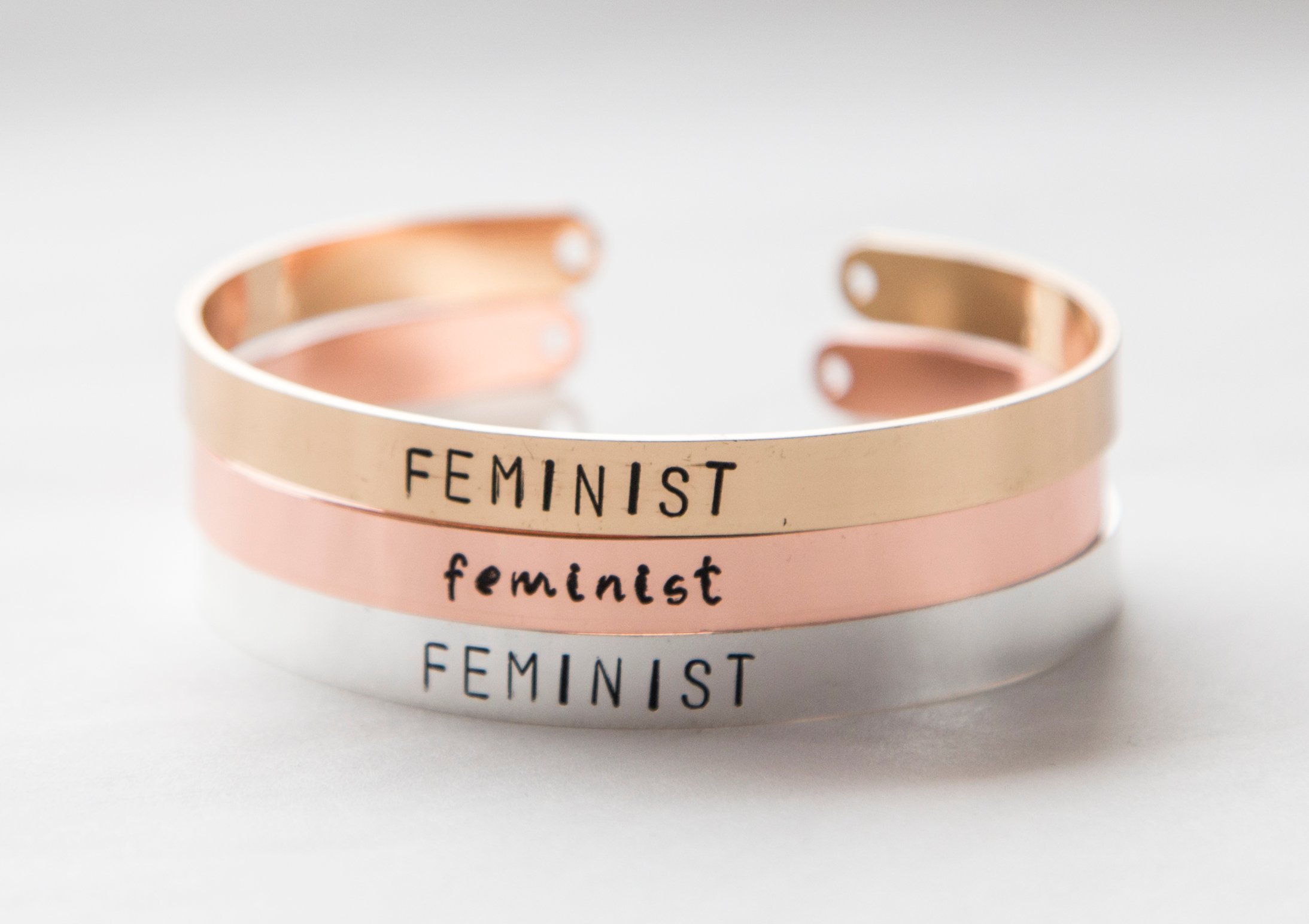 Hand-stamped gold plated cuff bracelet with feminist message, adjustable size, available in rose gold, gold, and silver finishes.