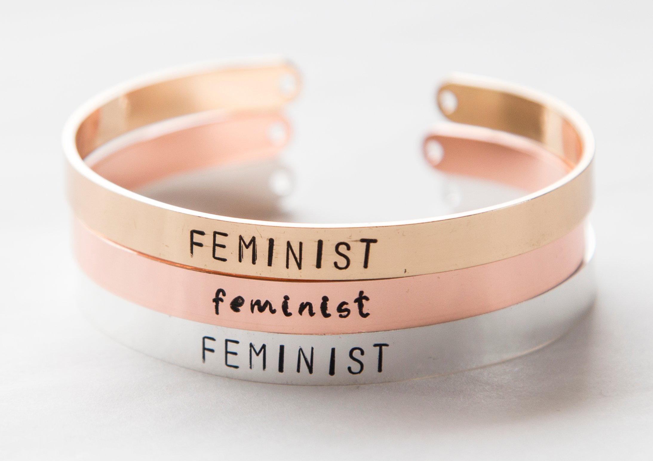 Hand-stamped gold plated cuff bracelet with feminist message, adjustable size, available in rose gold, gold, and silver finishes.