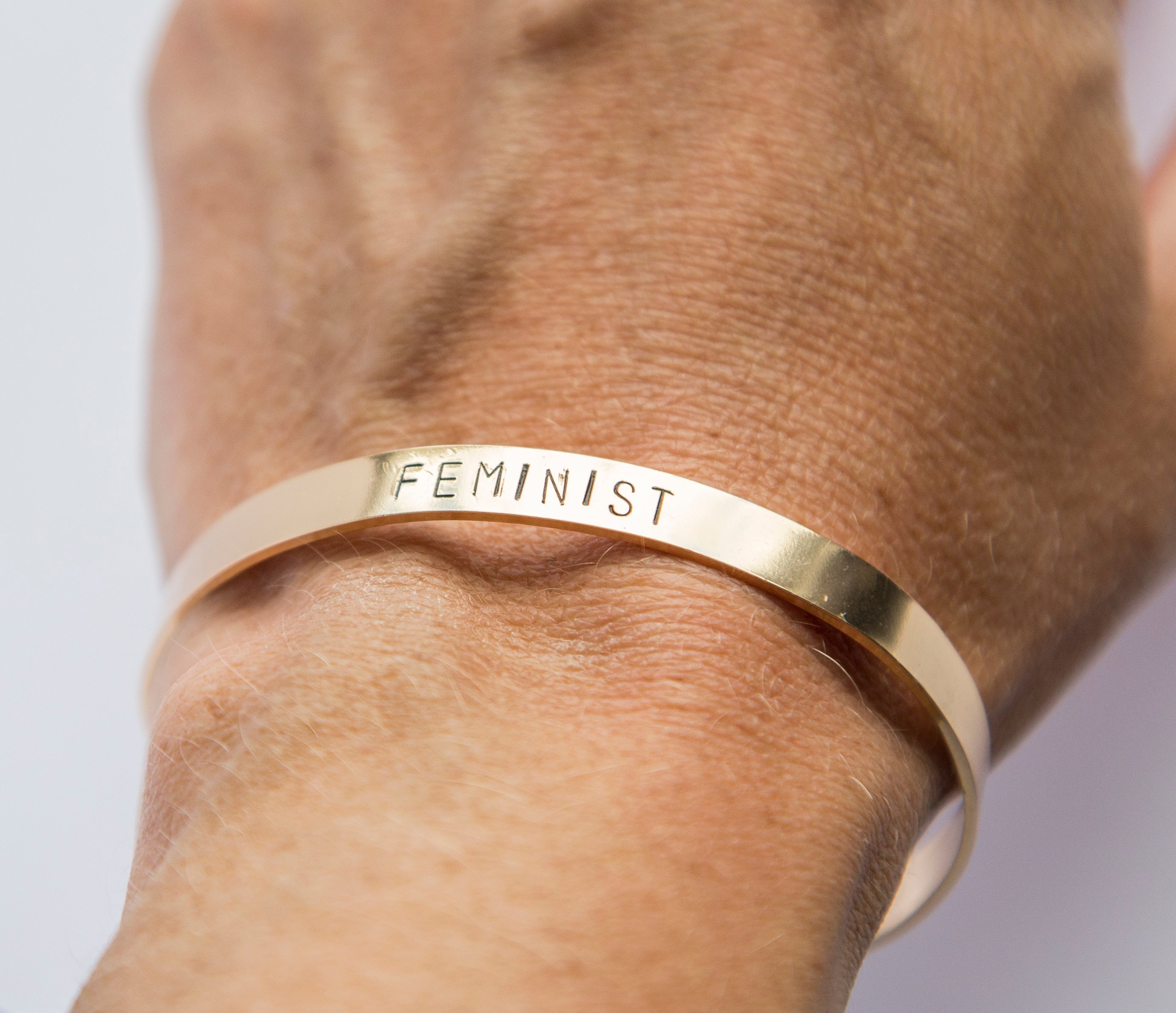 Hand-stamped gold plated cuff bracelet with feminist message, adjustable size, available in rose gold, gold, and silver finishes.