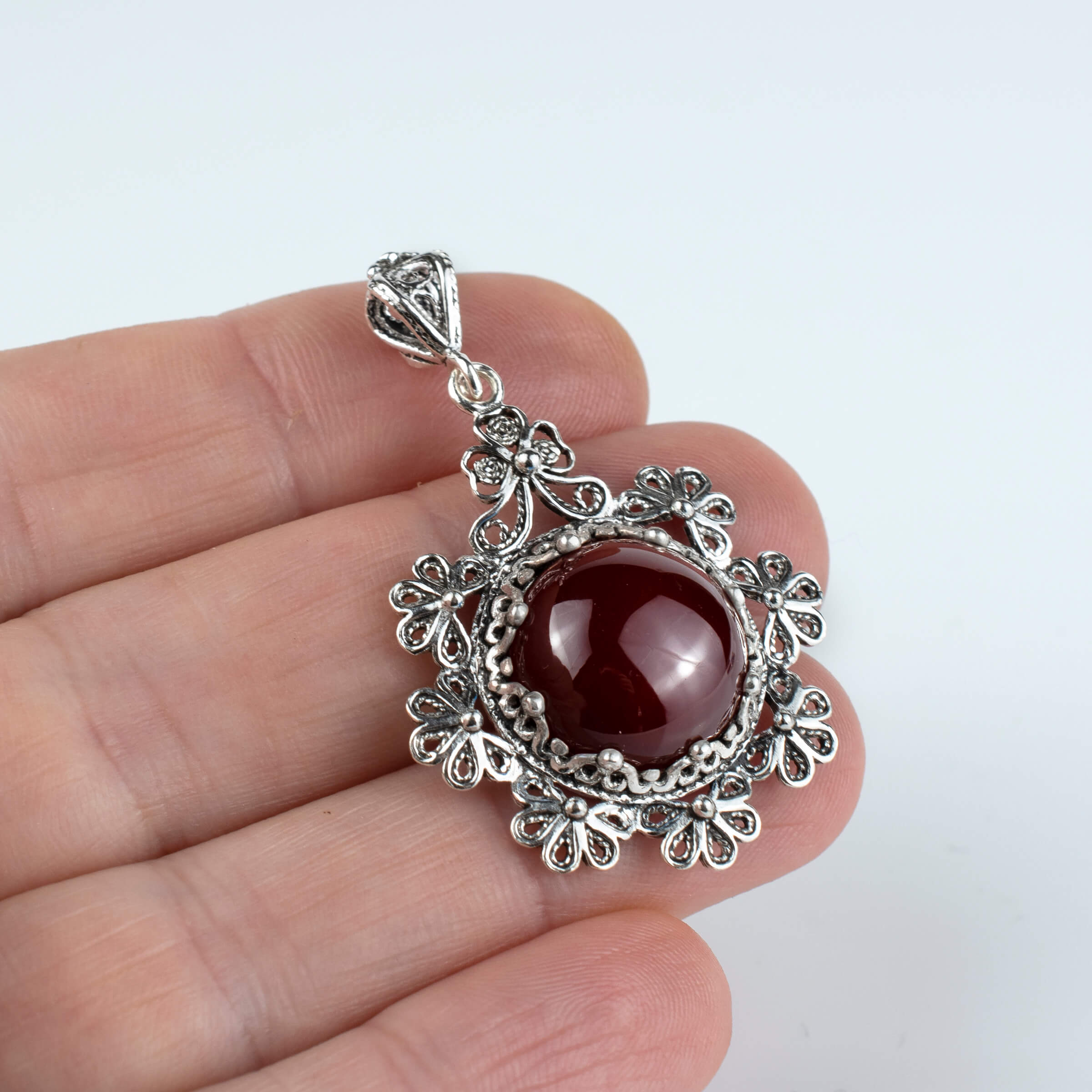 Sterling silver filigree pendant featuring a round cut carnelian gemstone in a floral design, showcasing intricate metalwork.