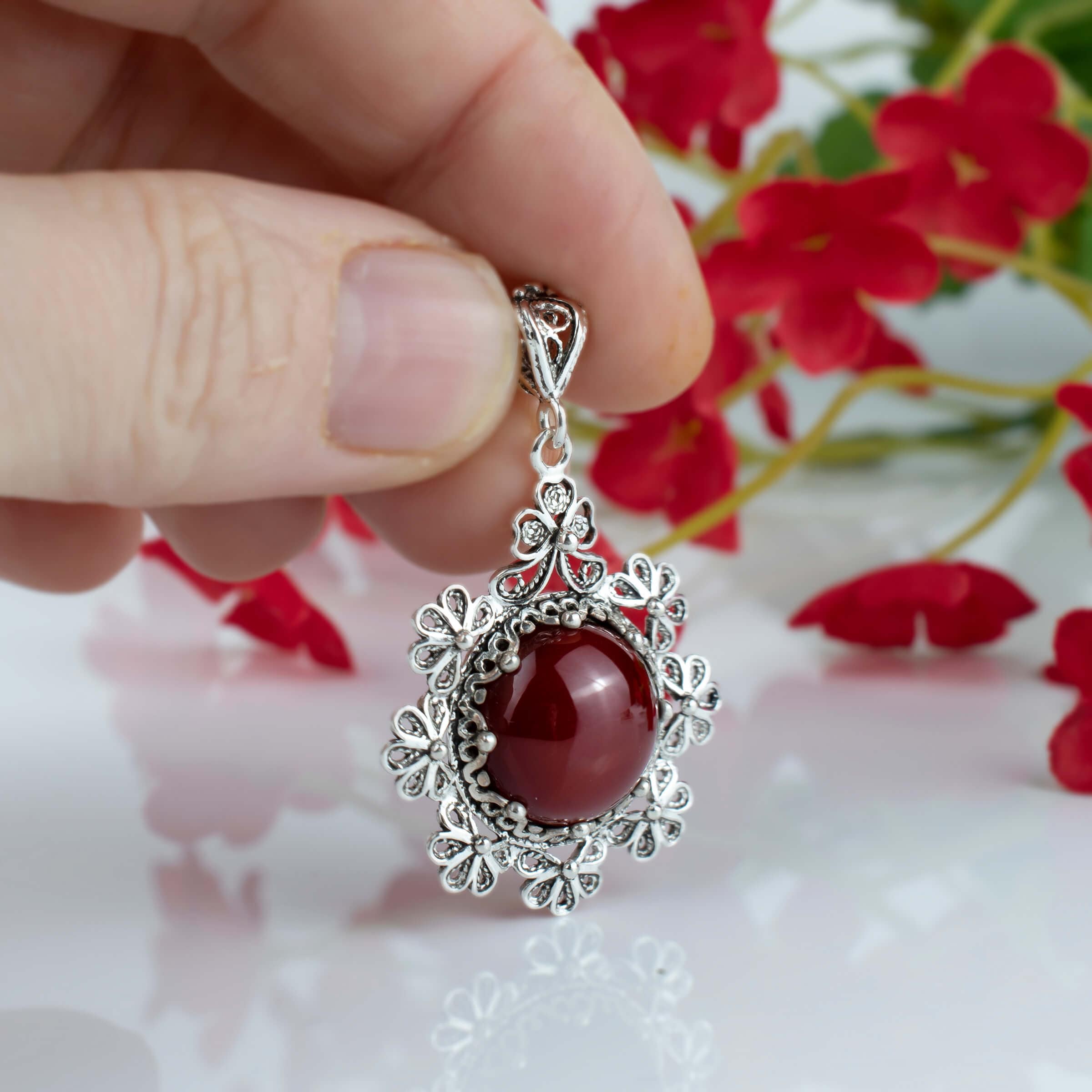 Sterling silver filigree pendant featuring a round cut carnelian gemstone in a floral design, showcasing intricate metalwork.