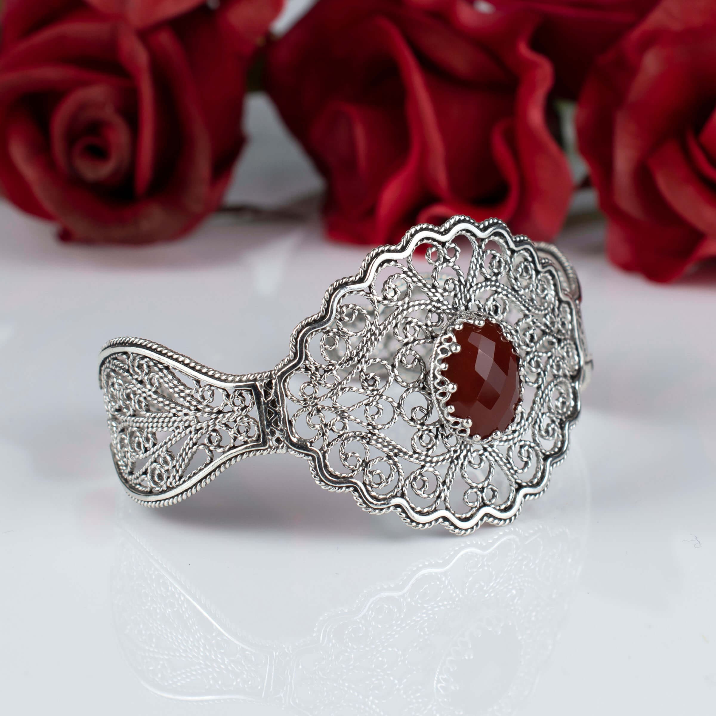 Elegant sterling silver cuff bracelet featuring intricate filigree design and a faceted carnelian gemstone.