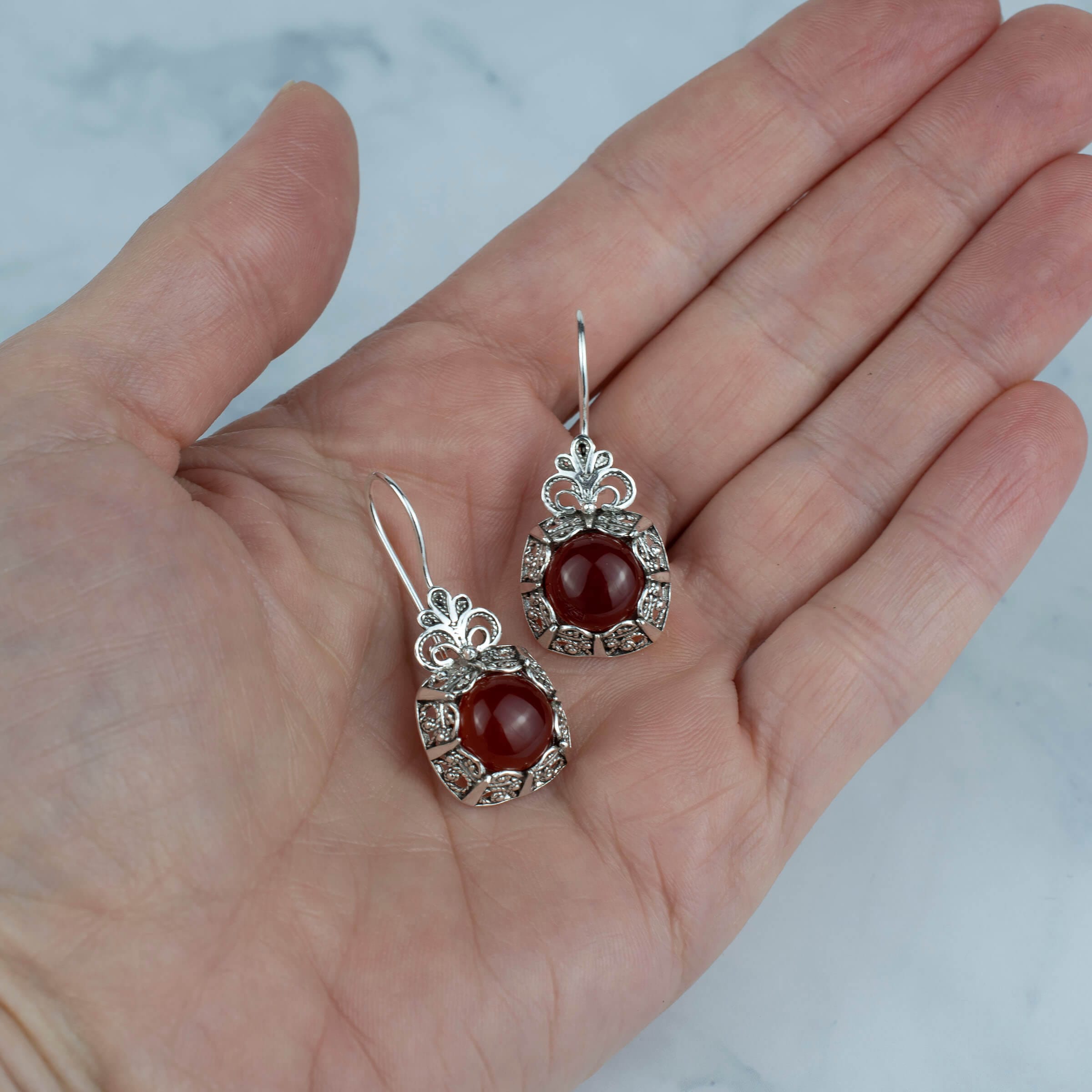 Elegant handmade silver drop earrings featuring intricate filigree design and a vibrant carnelian gemstone.
