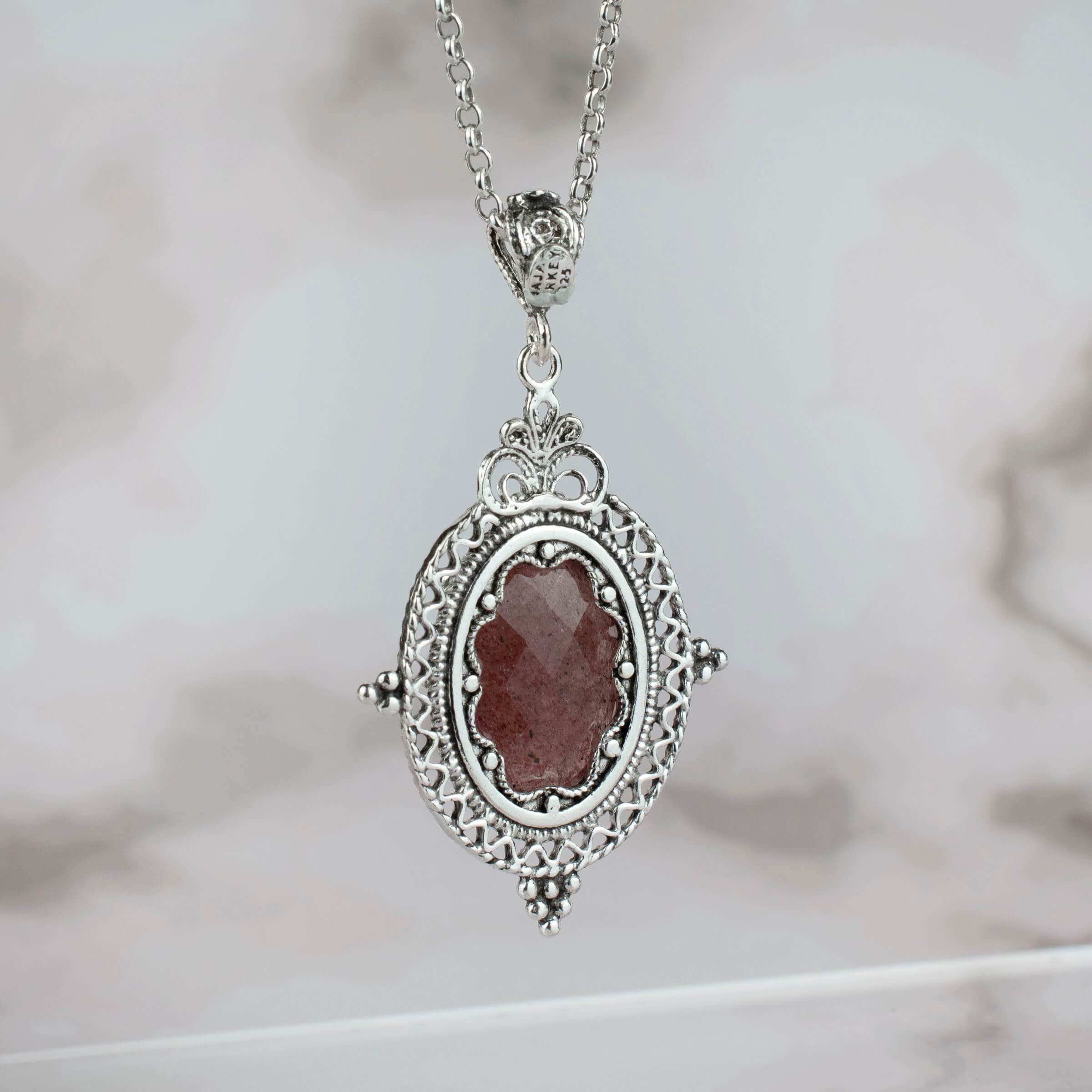 Elegant silver oval pendant necklace featuring filigree art and a cherry quartz gemstone, showcasing intricate craftsmanship.