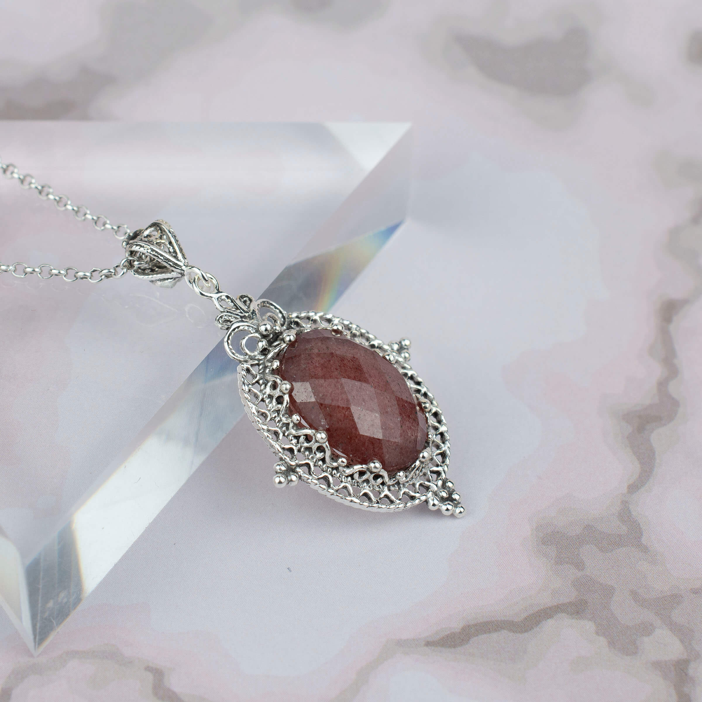 Elegant silver oval pendant necklace featuring filigree art and a cherry quartz gemstone, showcasing intricate craftsmanship.