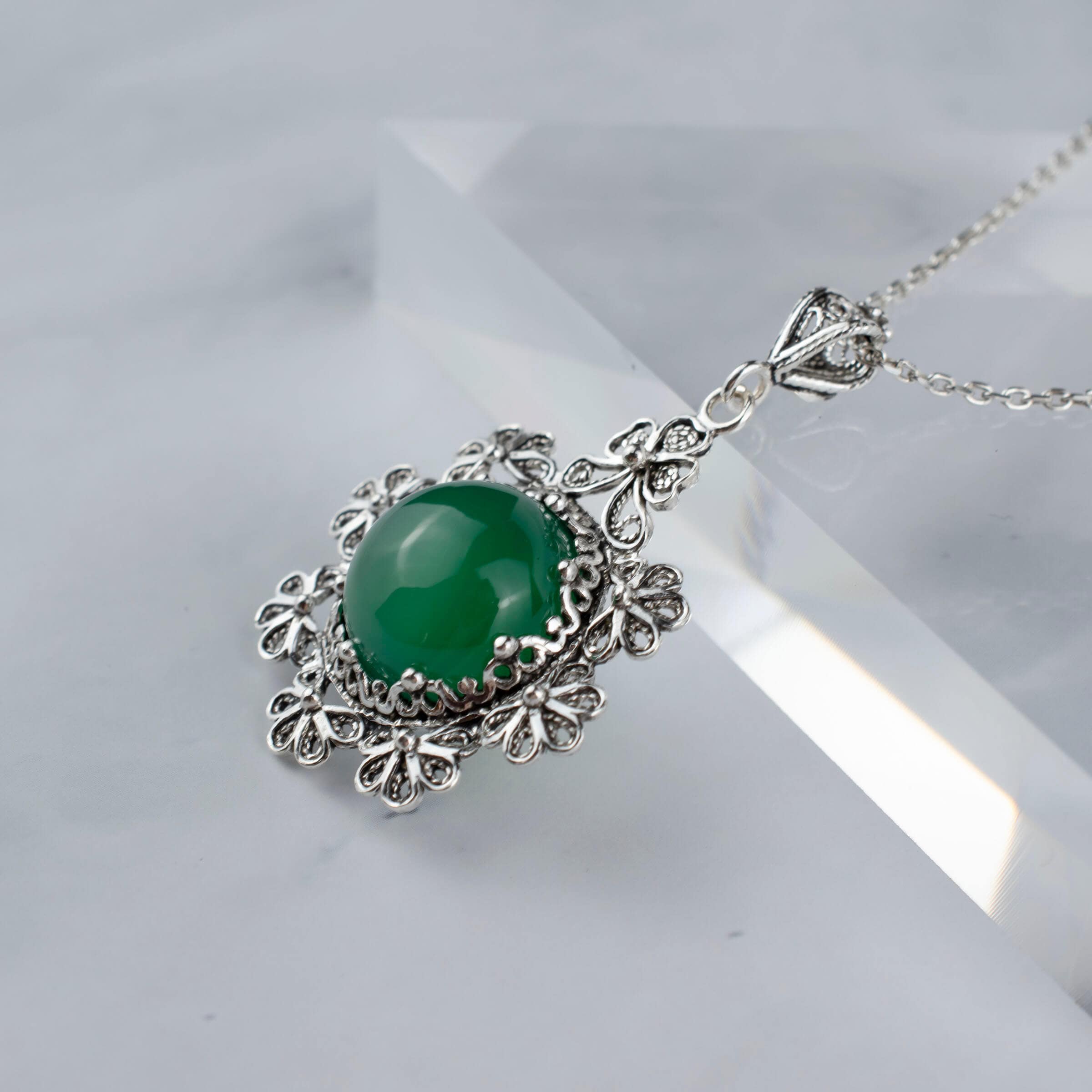 Sterling silver filigree pendant featuring a green agate gemstone in a floral design, showcasing intricate craftsmanship.