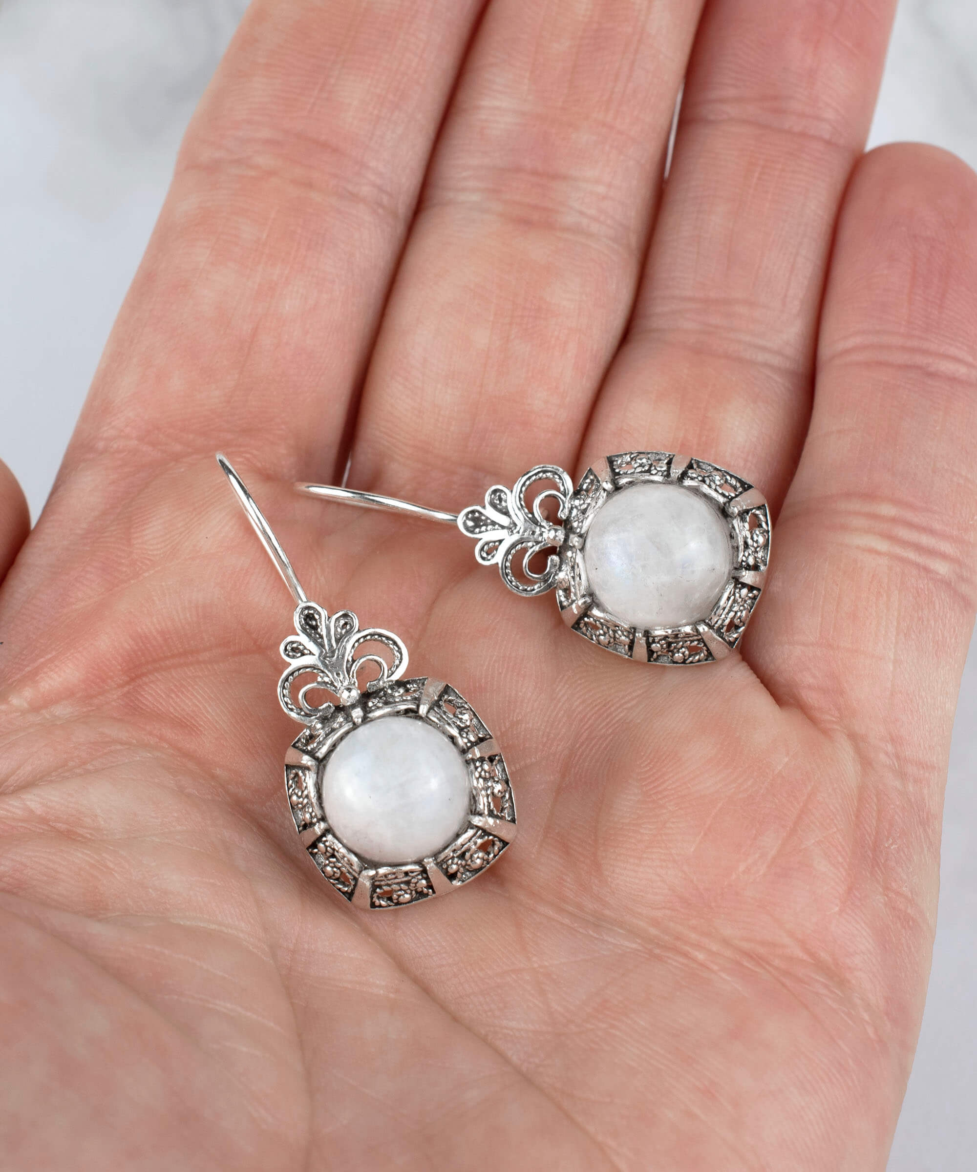 Elegant sterling silver drop earrings featuring a round-cut moonstone gemstone in a delicate filigree design.