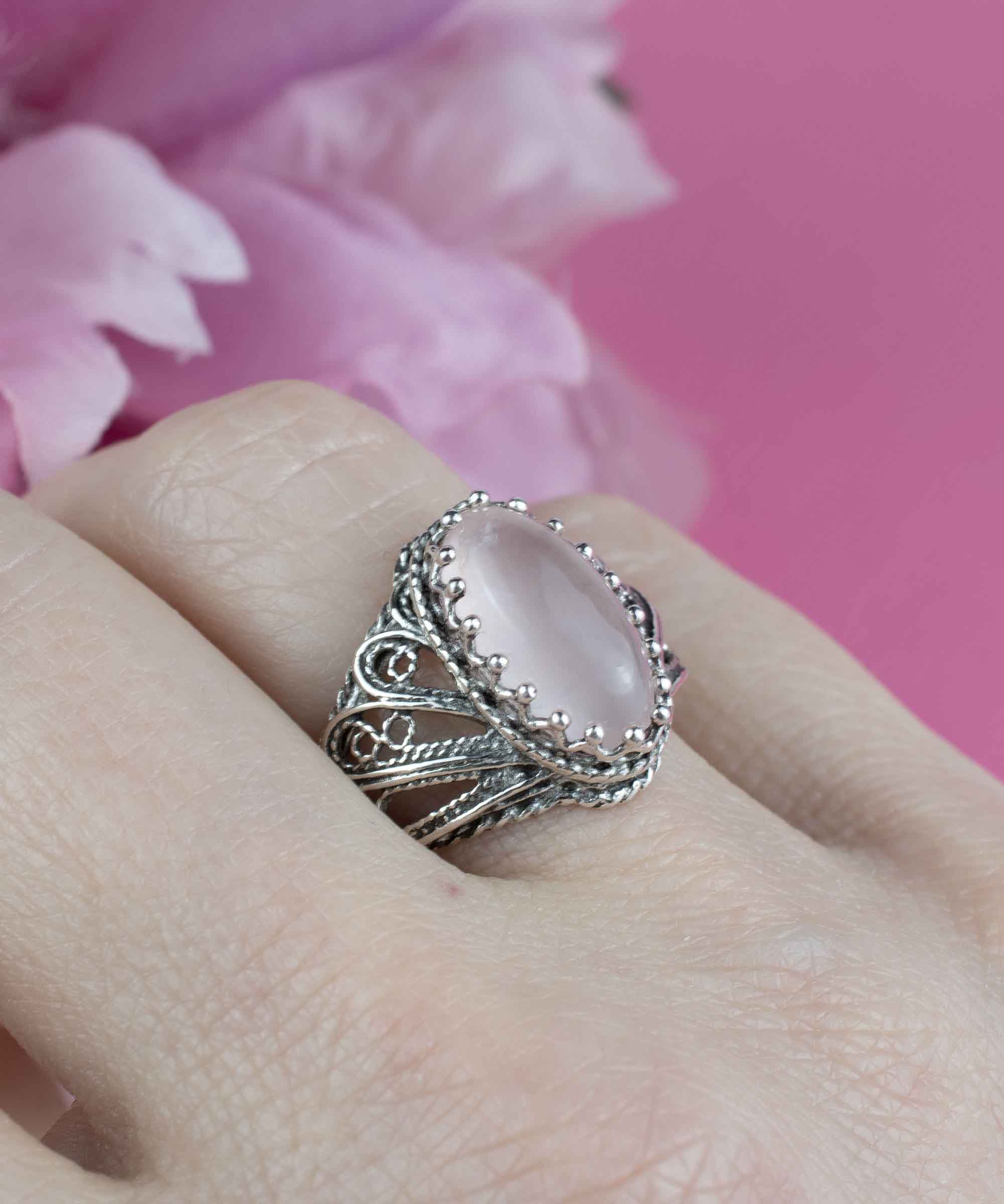 Elegant silver cocktail ring featuring intricate filigree design and a rose quartz gemstone in angel wings setting.