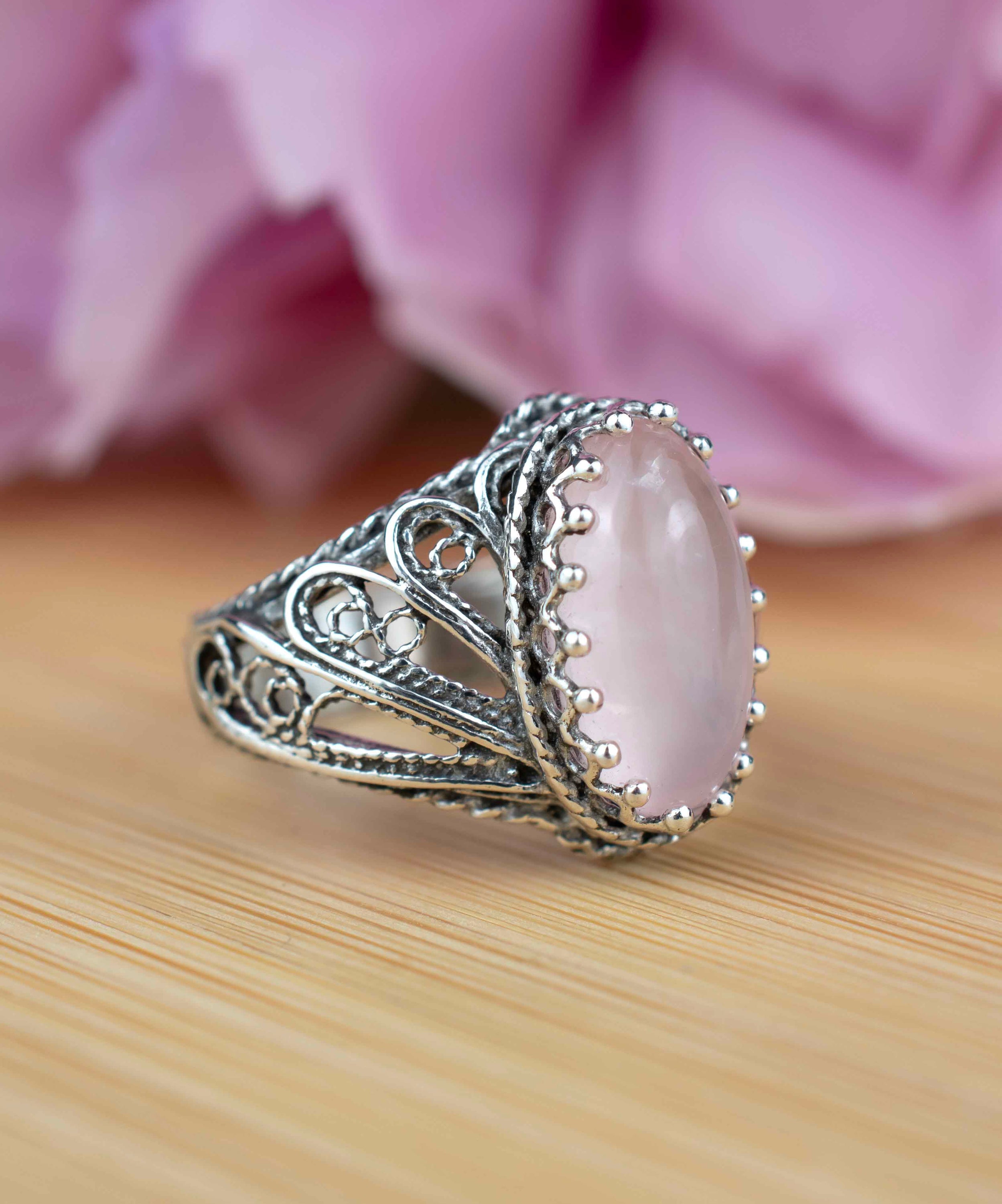 Elegant silver cocktail ring featuring intricate filigree design and a rose quartz gemstone in angel wings setting.