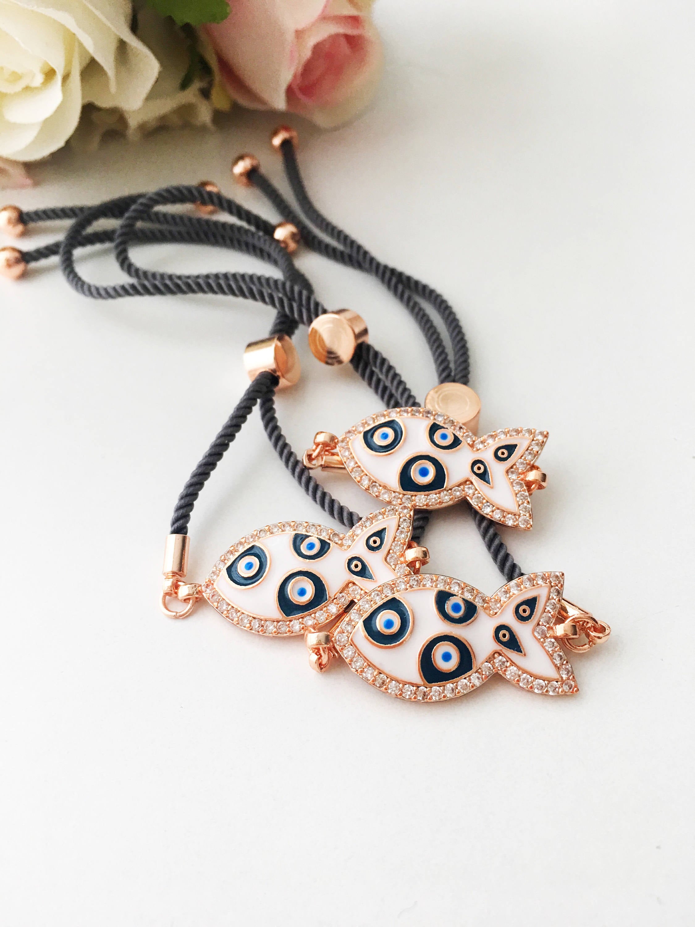 A stylish Fish Charm Bracelet featuring a rose gold plated evil eye charm on an adjustable string, perfect for everyday wear.