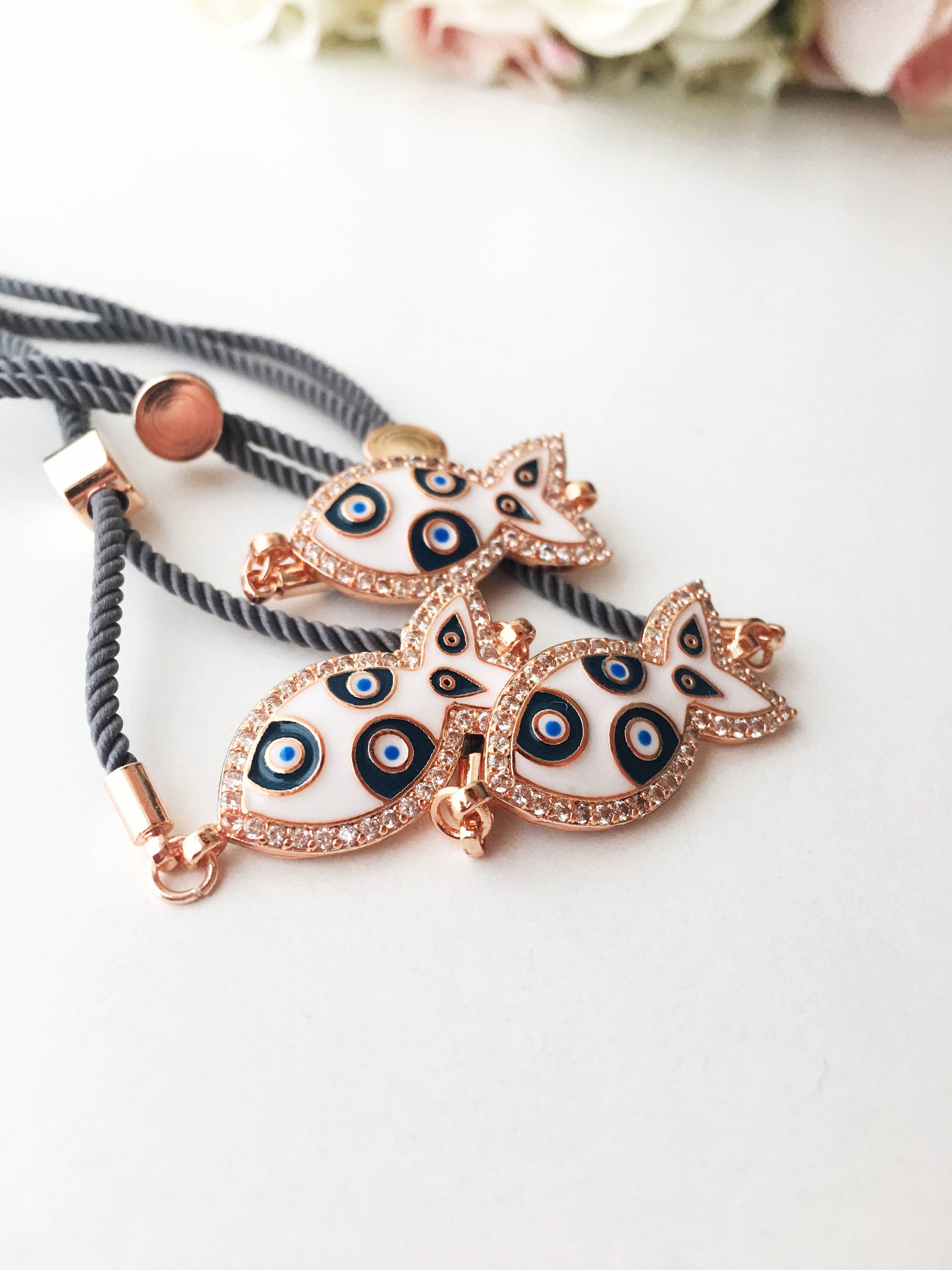 A stylish Fish Charm Bracelet featuring a rose gold plated evil eye charm on an adjustable string, perfect for everyday wear.