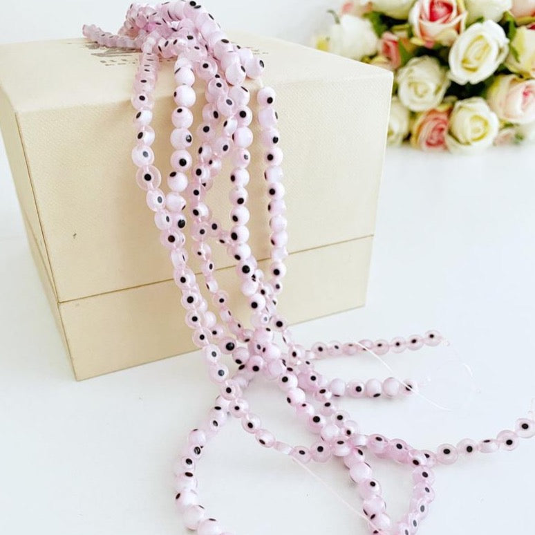 Flat round pale pink evil eye beads in various sizes from 6mm to 12mm, displayed on a white background.