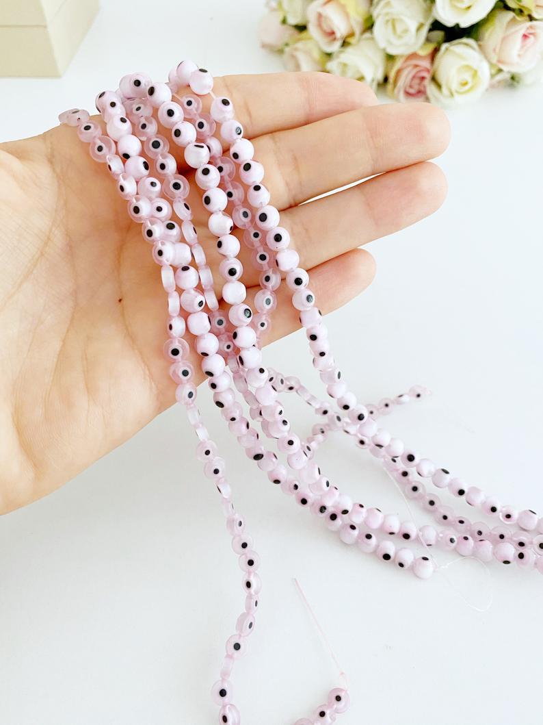 Flat round pale pink evil eye beads in various sizes from 6mm to 12mm, displayed on a white background.