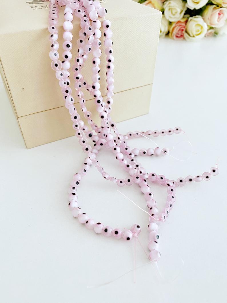 Flat round pale pink evil eye beads in various sizes from 6mm to 12mm, displayed on a white background.