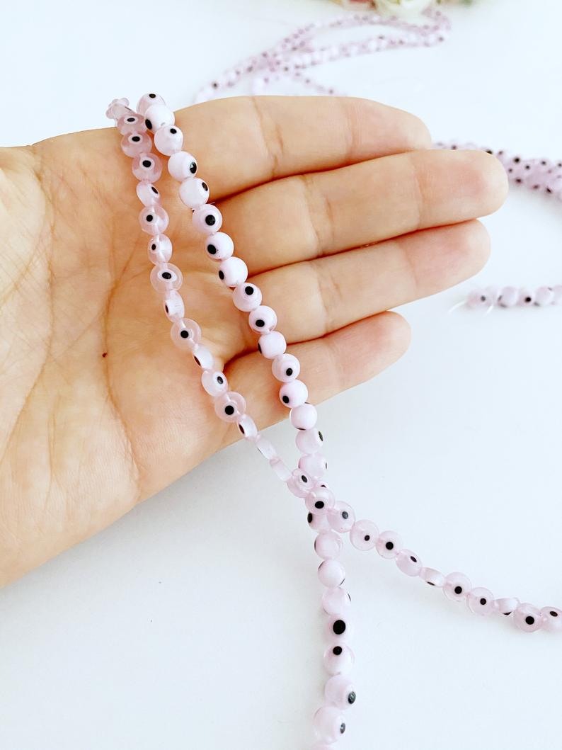 Flat round pale pink evil eye beads in various sizes from 6mm to 12mm, displayed on a white background.