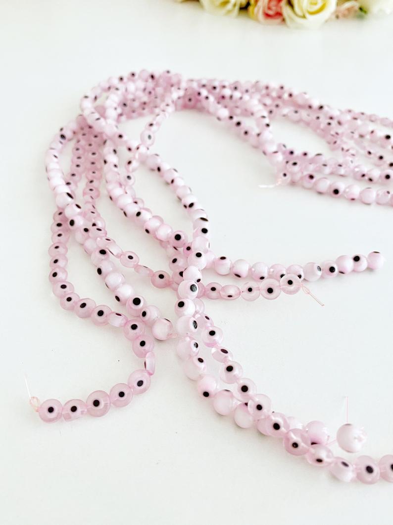 Flat round pale pink evil eye beads in various sizes from 6mm to 12mm, displayed on a white background.